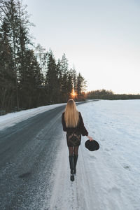 Full length of woman walking on snow covered road during sunset