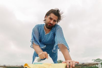 Low angle view of man ironing cloth against cloudy sky