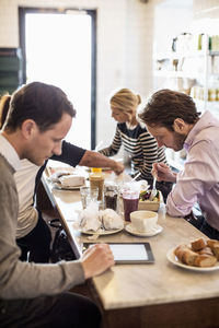 Mid adult businessman using digital tablet with colleagues having breakfast at restaurant table