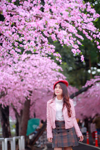 Full length of woman standing by pink flower tree