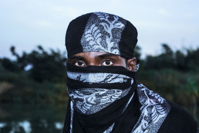 Close-up portrait of man covering face with scarf against sky