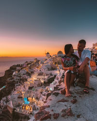 People sitting at beach against sky during sunset