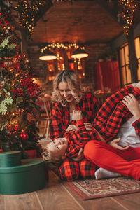 Smile active parents with small son in red checkered sleepwears waiting santa indoor.