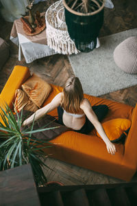 An overhead view of a woman sitting on a sofa in her home in a lotus position 