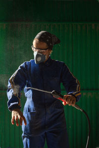 Concentrated female mechanic in uniform and mask checking air compressor gun before work