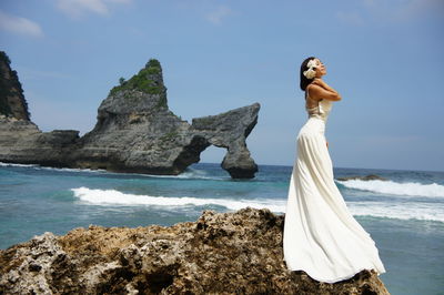 Woman standing on rock by sea against sky