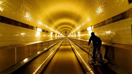 Rear view of man walking in illuminated tunnel