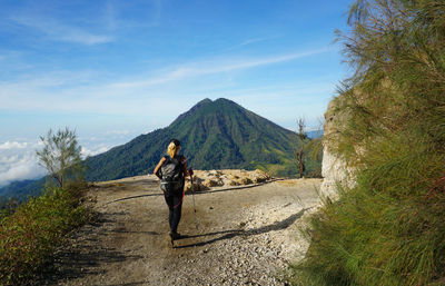 Rear view of woman standing on dirt road against sky