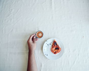 Cropped hand of man holding cup with coffee by pizza slice on table