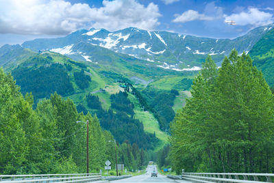 Road amidst trees and mountains against sky