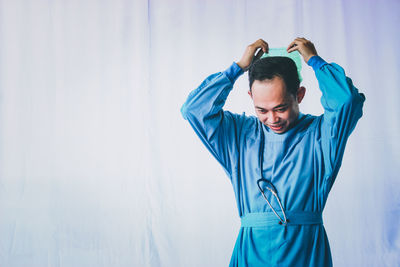 Young man looking away while standing against blue wall