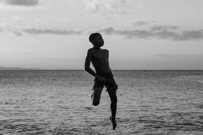 Full length of shirtless man standing in sea against sky