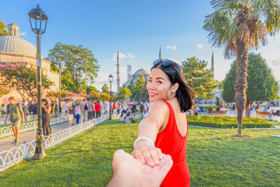 Portrait of smiling woman holding hands while standing in city