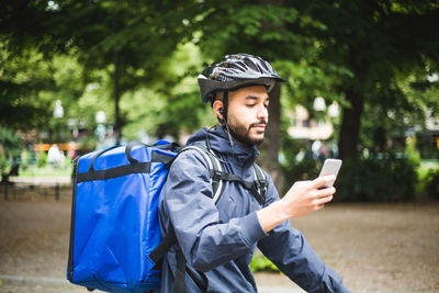 Young man using smart phone while sitting on tree