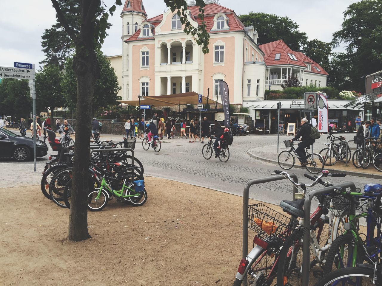 building exterior, bicycle, land vehicle, transportation, architecture, mode of transport, street, built structure, city, large group of people, parking, car, tree, parked, city life, men, stationary, person, outdoors