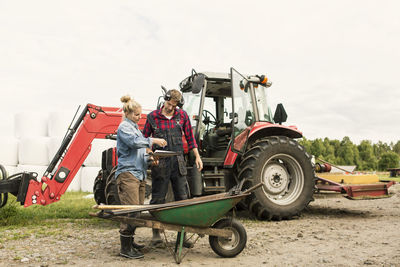 Woman showing document to male worker by tractor at farm