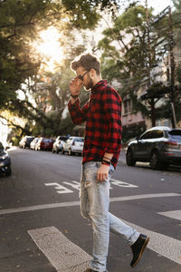 Man wearing plaid shirt and sunglasses while walking on road