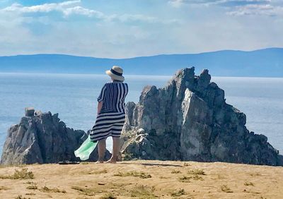 Rear view of man standing on rock by sea against sky