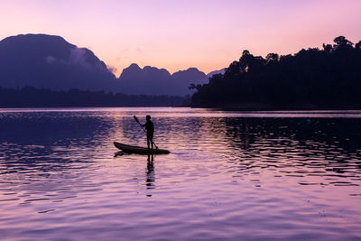 Silhouette man in lake against sky during sunset