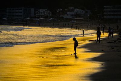 Silhouette people on beach against sky during sunset