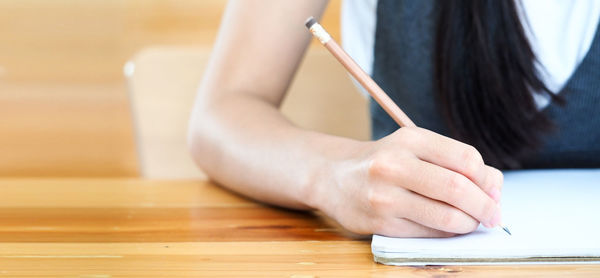 Midsection of woman writing in book at desk