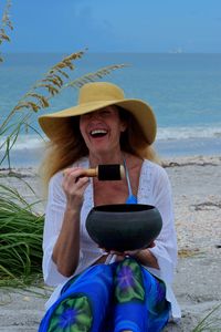 Cheerful woman holding singing bowl at beach