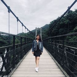 Full length portrait of woman on footbridge against sky