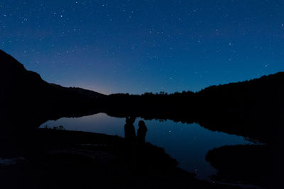 Silhouette people standing by lake against sky at night