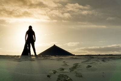 Silhouette man standing on beach against sky during sunset