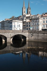 Arch bridge over river by buildings against sky