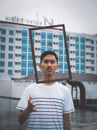 Portrait of young man throwing picture frame while standing on building terrace