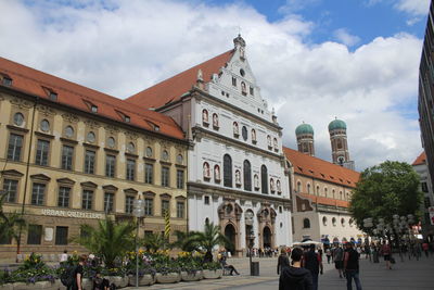 People on road by buildings in city against sky