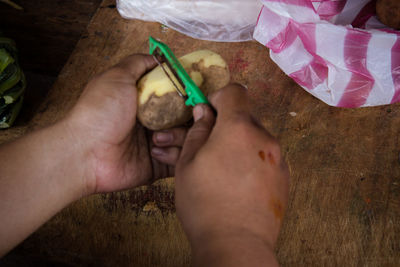 Cropped hands peeling potato over table