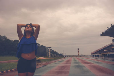 Beautiful woman standing on sports track against cloudy sky