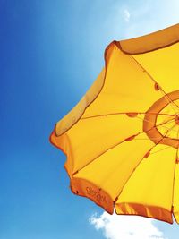 Low angle view of yellow parasol against blue sky