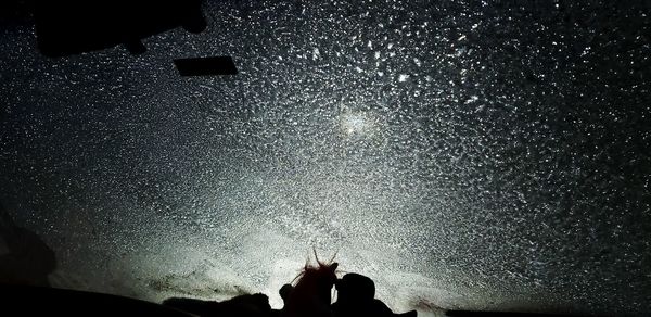 Low section of silhouette people standing against illuminated sky at night