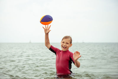 Portrait of happy girl with arms raised at sea against sky