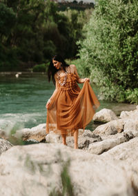 Rear view of woman sitting on rock dancing with her dress in nature like a mother nature