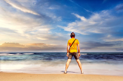 Rear view of man standing at beach during sunset