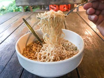 Close-up of hand holding noodles in bowl on table