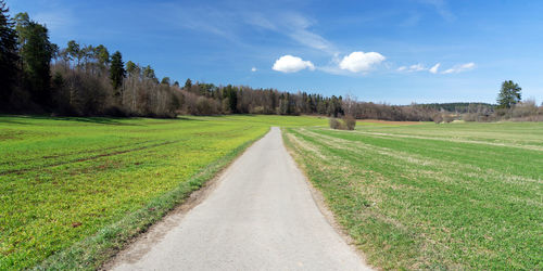 Dirt road amidst field against sky