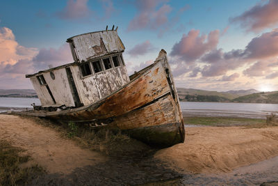 Abandoned boat on beach against sky