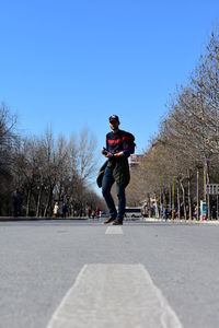 Man standing on road against clear blue sky