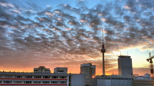Fernsehturm amidst buildings against cloudy sky during sunset