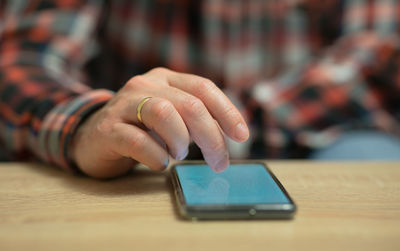 A man is reading news on his cell phone, which is lies on a wooden table