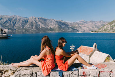 Woman sitting on sea by mountains against sky