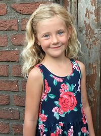 Portrait of smiling girl standing against brick wall