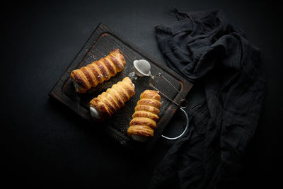 Baked tubules filled with whipped egg white cream on a black wooden kitchen board, top view