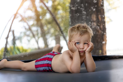Portrait of shirtless boy looking away while sitting on tree