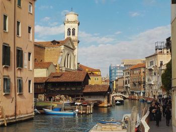 Boats in canal amidst buildings in city against sky